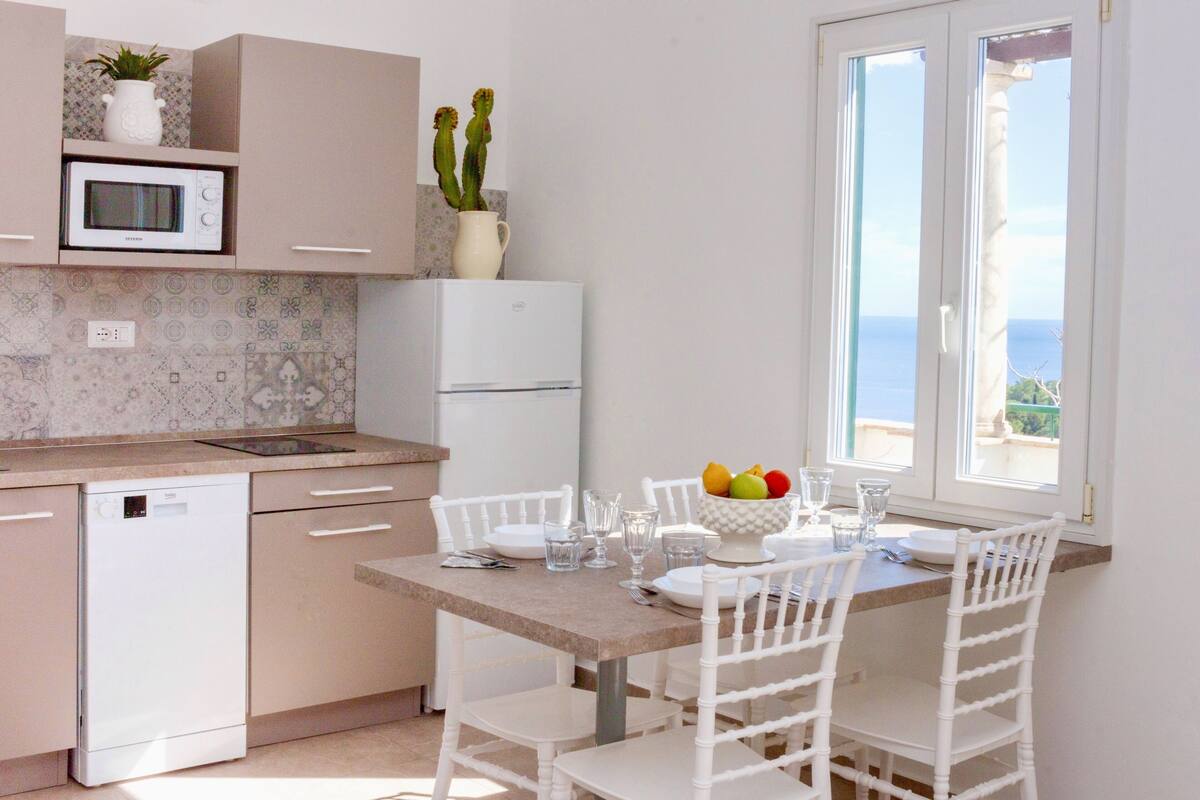 A kitchen with a dishwasher, microwave, and refrigerator. There is a dining table with chairs and a bowl of fruit.