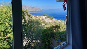 A view from a window overlooking a coastal town with buildings and a clear blue sea. - Residence Terra Rossa (Taormina)