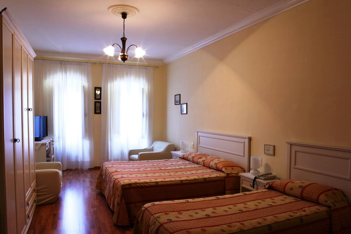 A hotel room with two beds, a desk with a chair, a television, and a chandelier.