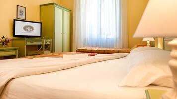 A hotel room with a bed, a desk with a computer, a wardrobe, and a window with curtains.