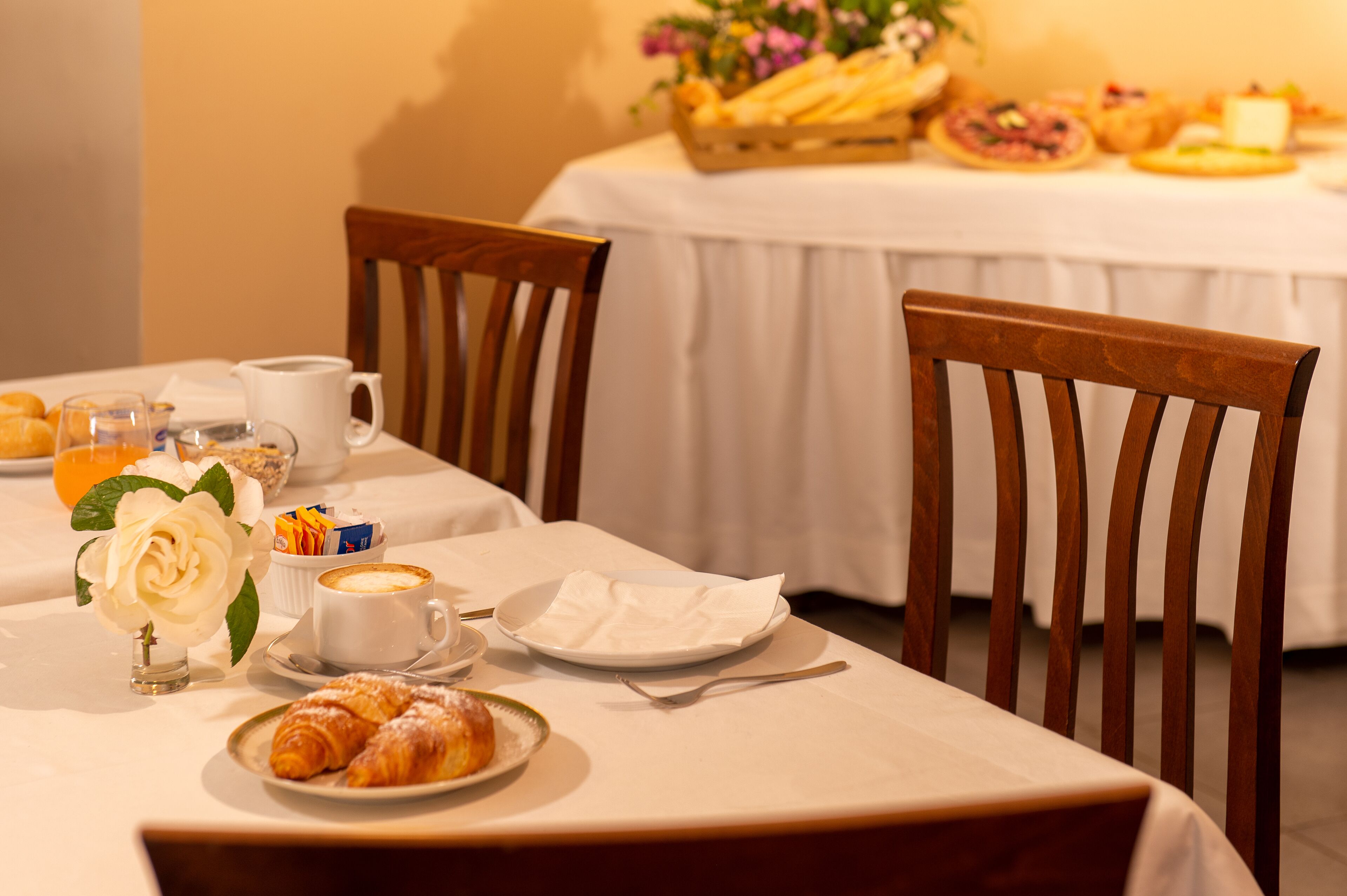 A breakfast setting with croissants, coffee, and juice on a table with white tablecloths.