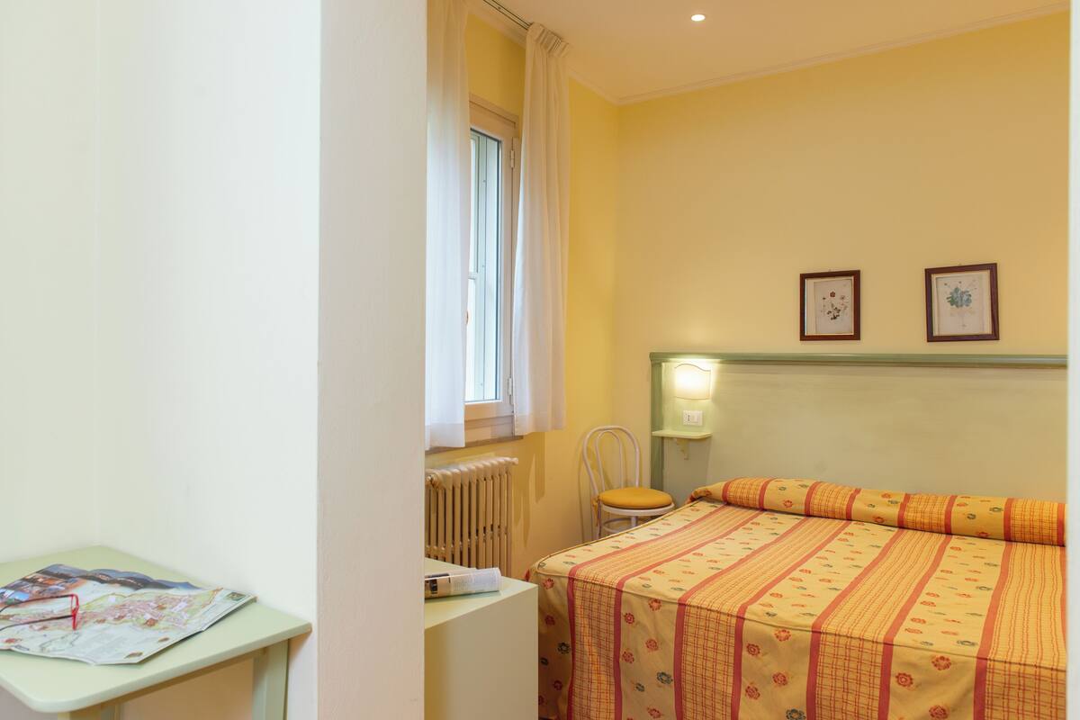 A bedroom with a bed, a chair, a table with a map, and two framed pictures on the wall.