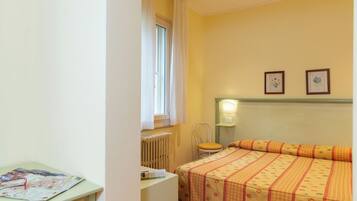 A bedroom with a bed, a chair, a table with a map, and two framed pictures on the wall.