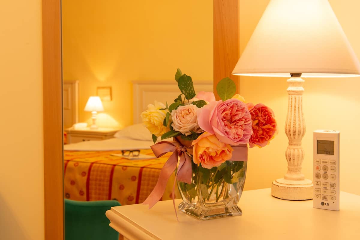 A bedside table with a vase of flowers, a lamp, and a digital clock.