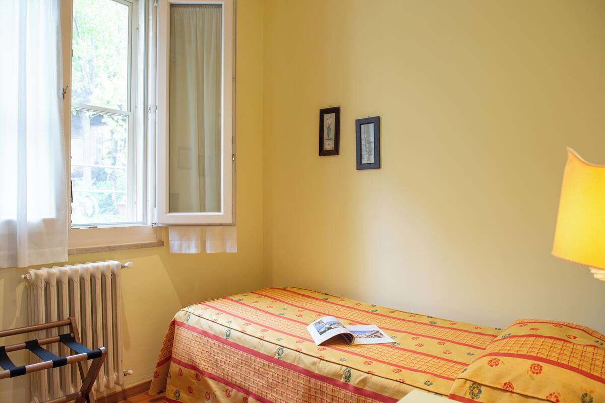 A small room with a bed, a window, a radiator, and a lamp.
