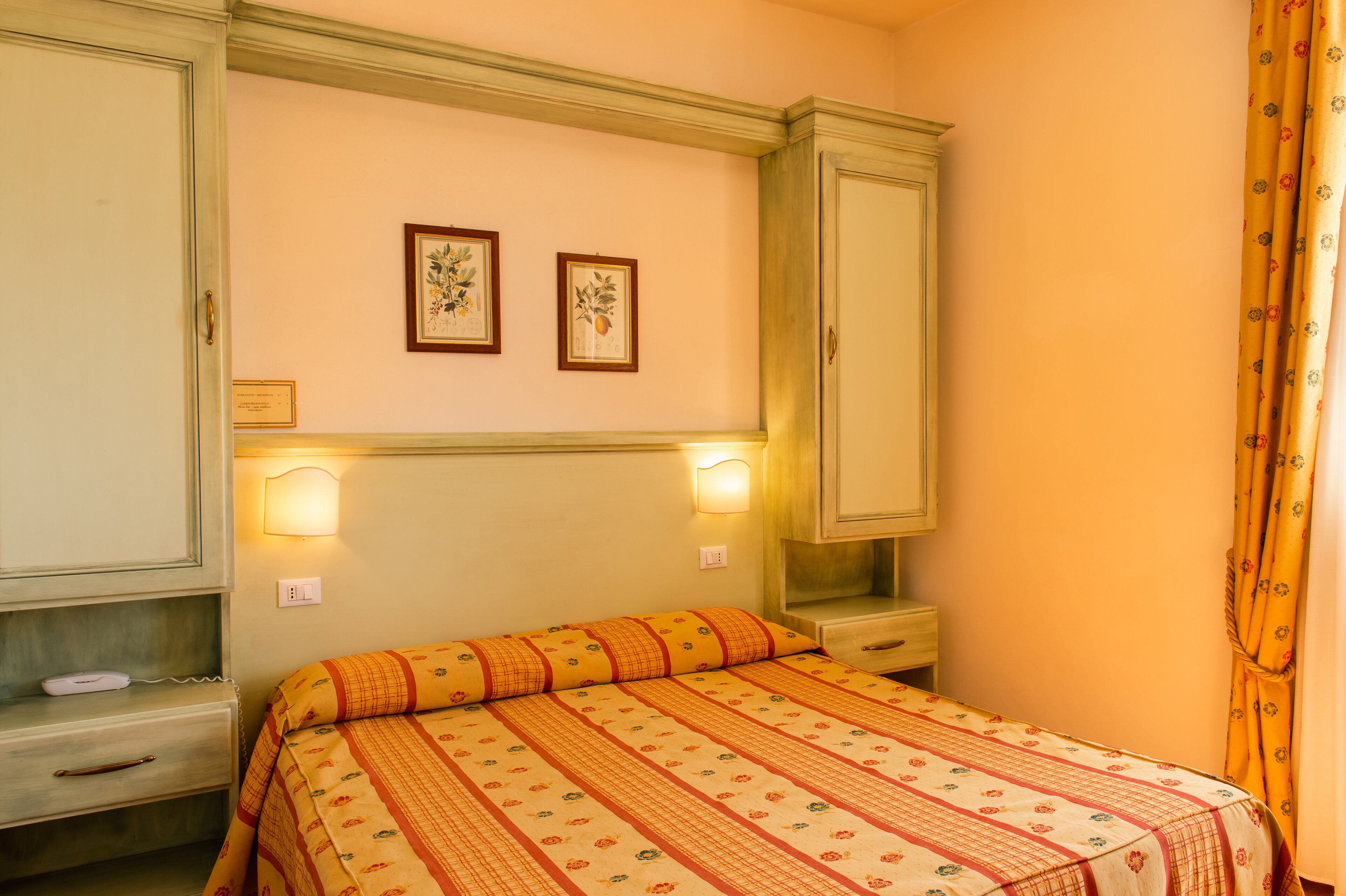 A bedroom with a bed, a wardrobe, a nightstand, and two wall-mounted lamps.