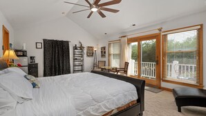 A bedroom with a large bed, a ceiling fan, a desk, and a balcony with a view of the outdoors. - Venus Studio: Hottub, King Bed, Kayak, Bikes, SUP,  (Kitty Hawk)