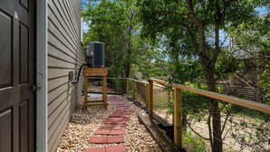 A pathway leading to a wooden deck with a metal air conditioning unit on a stand. - Venus Studio: Hottub, King Bed, Kayak, Bikes, SUP,  (Kitty Hawk)