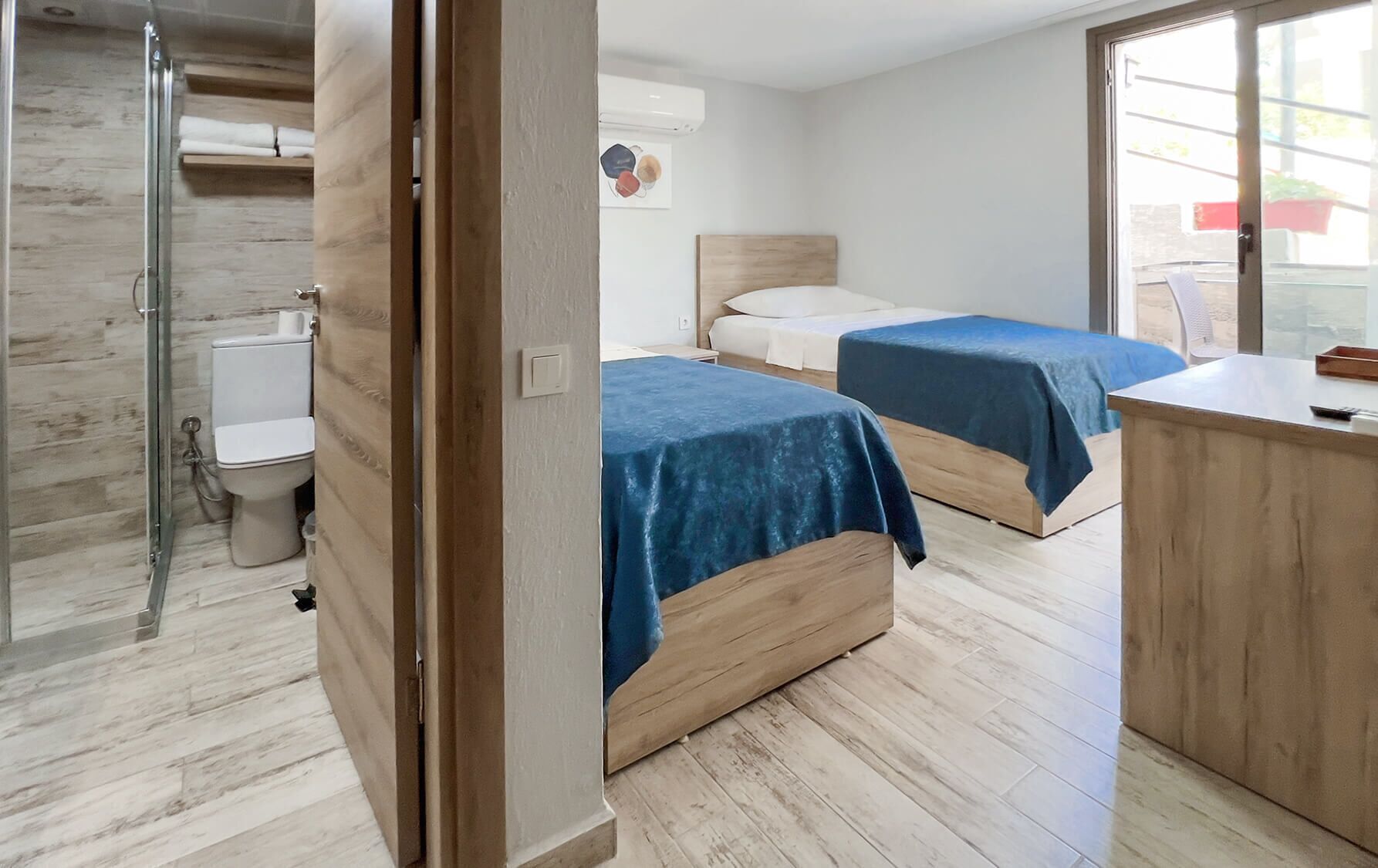 Una habitación de hotel con dos camas, ducha y suelo de madera.