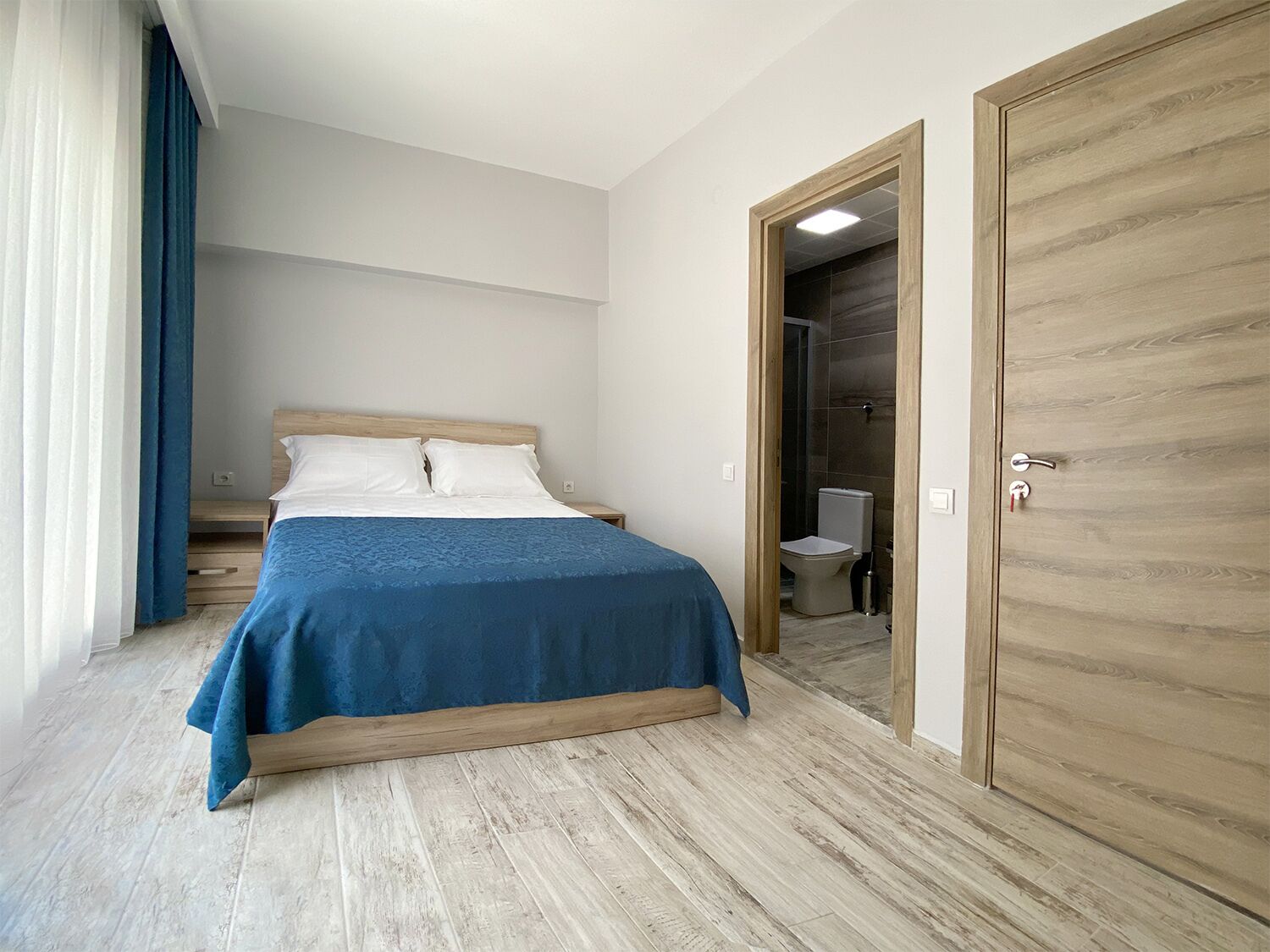 Ein Schlafzimmer mit einem Bett, einem Holzschrank und einem durch eine offene Tür einsehbaren Badezimmer.