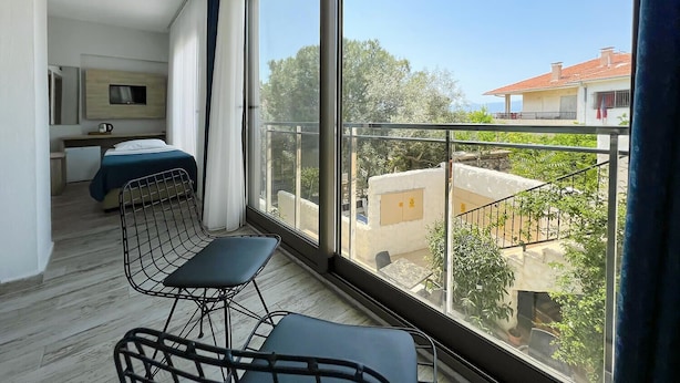 Un balcon donnant sur un quartier résidentiel, un lit, une petite kitchenette et une chaise.