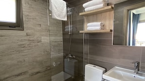 Une salle de bain moderne avec une douche à parois de verre, des toilettes, un lavabo et une étagère en bois où sont posées des serviettes.