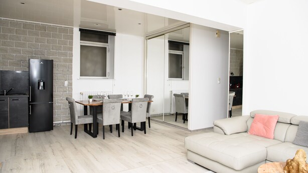 A modern kitchen with a black refrigerator, a dining area with a table and chairs, and a living room with a beige sofa and a coffee table. - SPACIOUS, EXCEPTIONAL APARTMENT (Épinal)