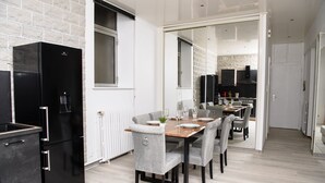 A modern kitchen with a black refrigerator, white cabinetry, and a dining area with a wooden table and grey upholstered chairs. - SPACIOUS, EXCEPTIONAL APARTMENT (Épinal)
