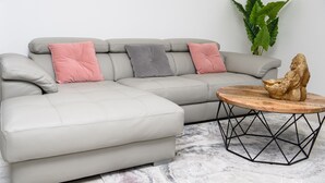 A light grey sectional sofa with three cushions in pink, grey, and pink. A round wooden coffee table with a gold sculpture sits in front. - SPACIOUS, EXCEPTIONAL APARTMENT (Épinal)