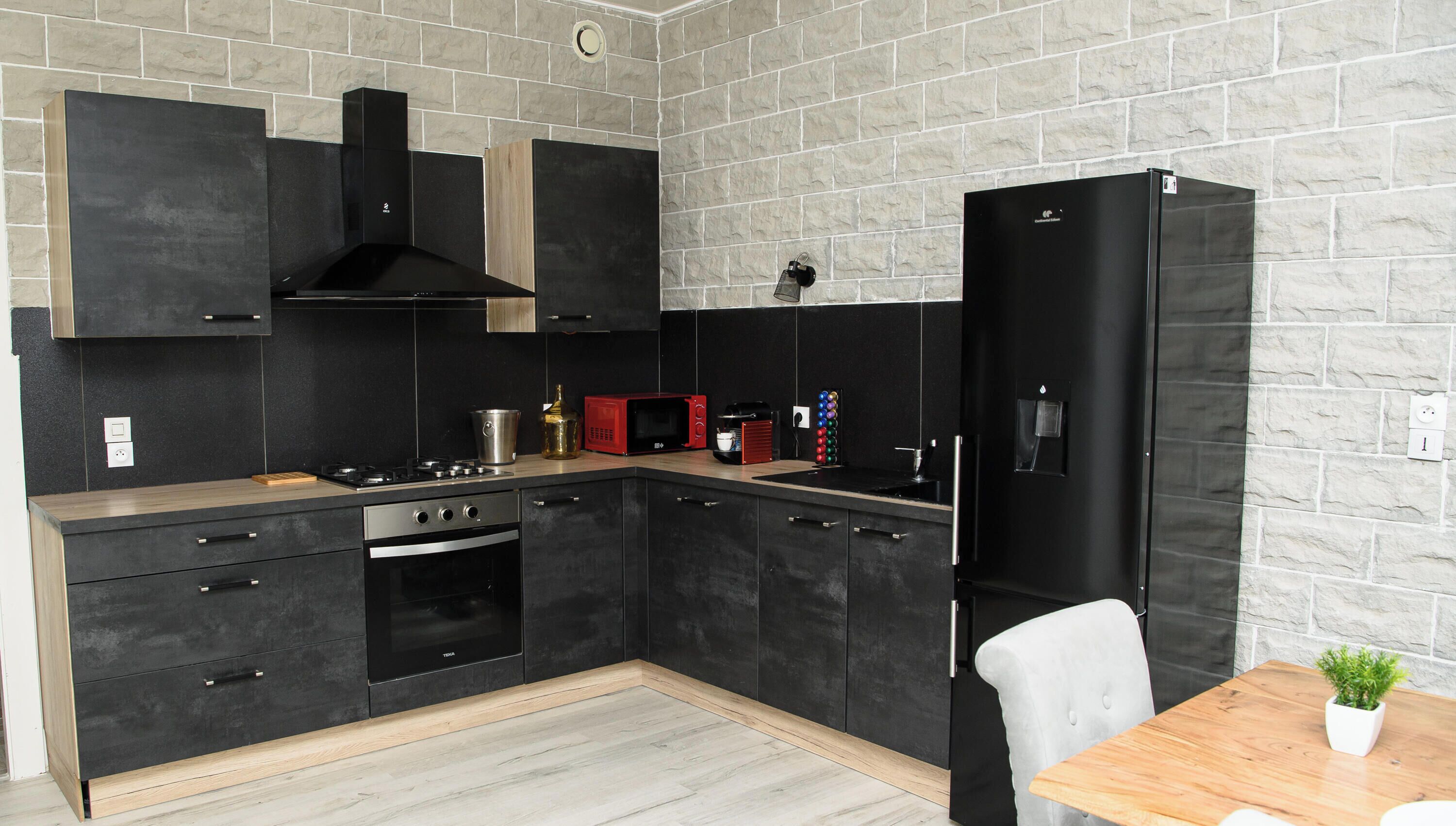 Eine moderne Küche mit schwarzen Schränken, einer Holzarbeitsplatte, einem schwarzen Kühlschrank und einem Esstisch mit einem Blumentopf.