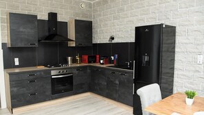 A modern kitchen with black cabinets, a wooden countertop, a black refrigerator, and a dining table with a potted plant. - SPACIOUS, EXCEPTIONAL APARTMENT (Épinal)