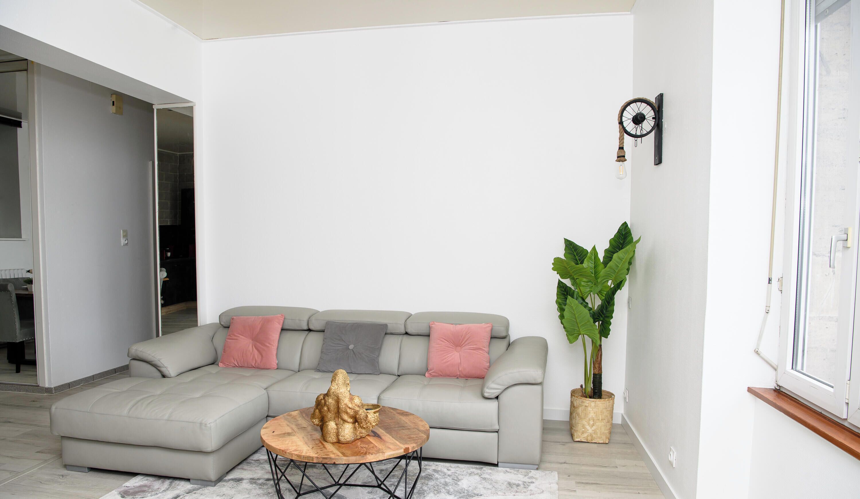 A living room with a sectional sofa, a round wooden coffee table, and a large potted plant.
