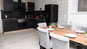 A modern kitchen with black cabinets, a wooden dining table, and grey upholstered chairs. - SPACIOUS, EXCEPTIONAL APARTMENT (Épinal)