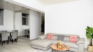 A modern living room with a grey sofa, a dining table with chairs, and a large window. - SPACIOUS, EXCEPTIONAL APARTMENT (Épinal)