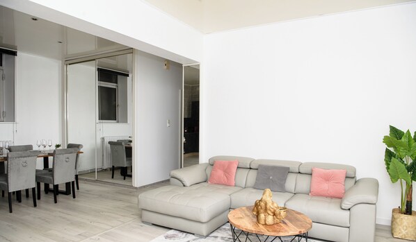 A modern living room with a grey sofa, a dining table with chairs, and a large window. - SPACIOUS, EXCEPTIONAL APARTMENT (Épinal)