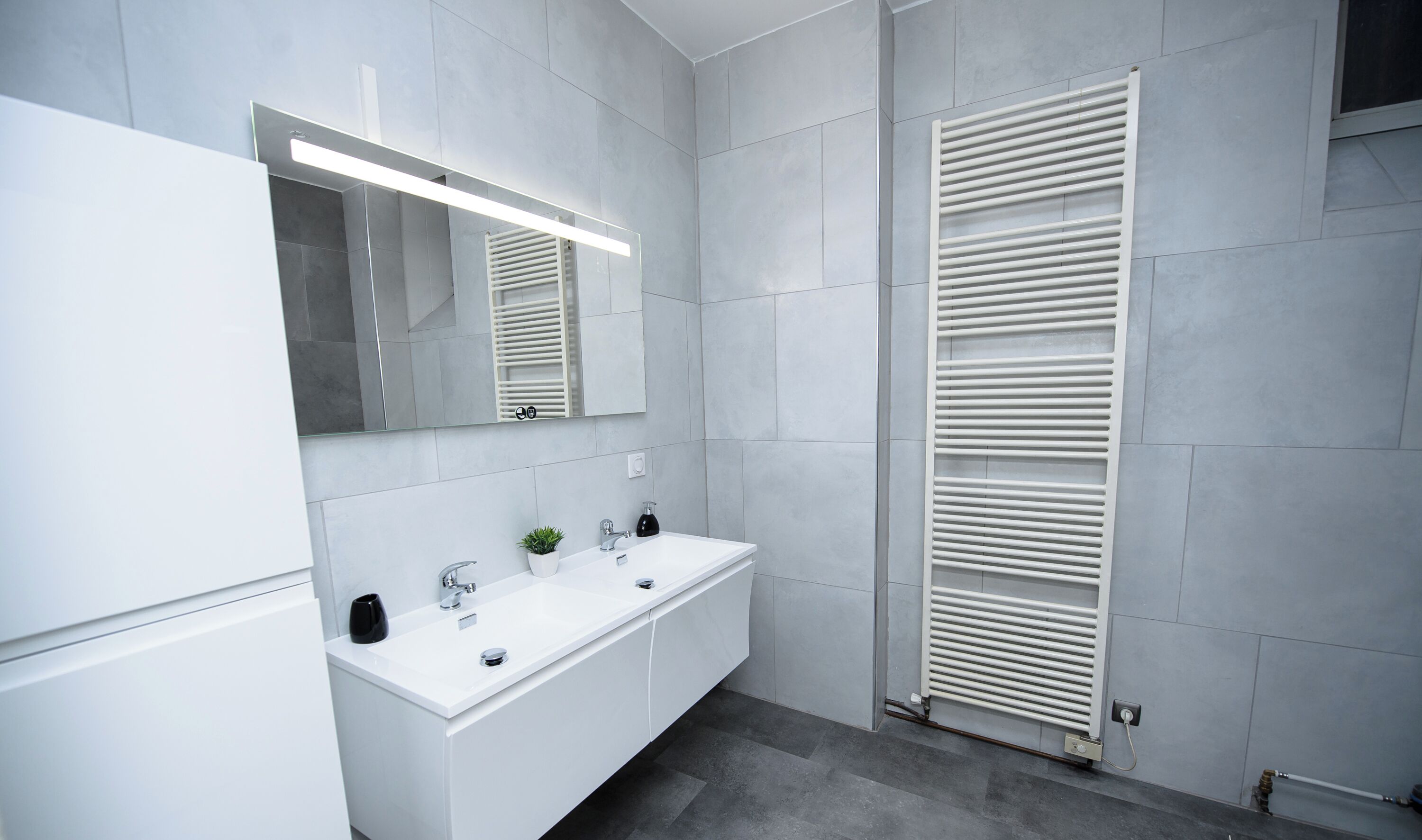 Un baño moderno con un tocador blanco, un espejo, un perchero y un radiador.