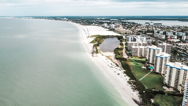An aerial view of a coastal area with a beach, a small lake, and high-rise buildings. - ELEVATE IN THE SUN! A Renovated Beachfront Condo! (Fort Myers Beach)