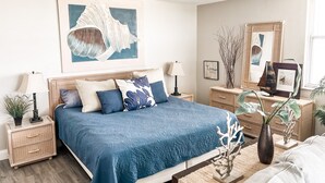 A bedroom with a bed, nightstands, a dresser, a mirror, and wall art. - ELEVATE IN THE SUN! A Renovated Beachfront Condo! (Fort Myers Beach)