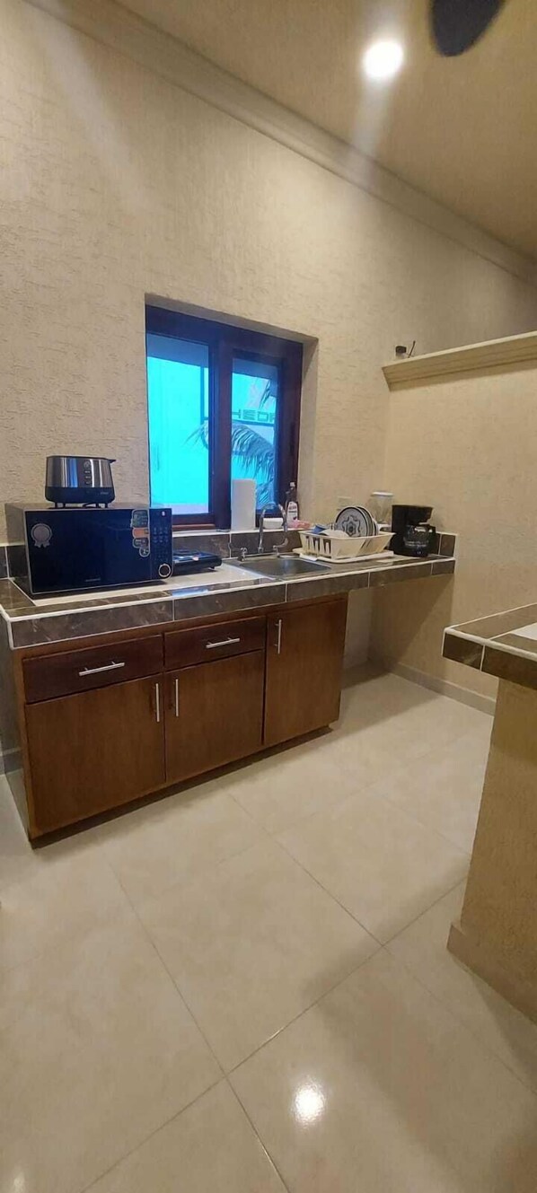 A kitchen with a large island, a microwave, a kettle, and a window with a view.