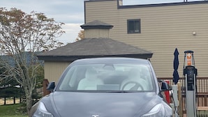 A Tesla Model 3 parked in a charging station area with a residential building in the background. - APPresSki - 5 bed Ski in Ski out - 50 Steps to Ski Sugar Mountain Slopes (Sugar Mountain)