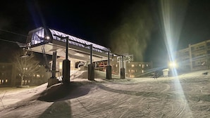 A snow-covered parking lot with a building featuring a glass facade and a ski lift. - APPresSki - 5 bed Ski in Ski out - 50 Steps to Ski Sugar Mountain Slopes (Sugar Mountain)