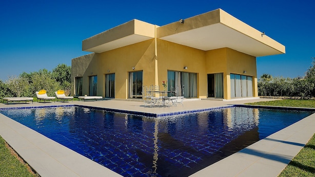 Une maison moderne à deux étages, dotée d’une piscine, de grandes fenêtres et de mobilier d’extérieur.