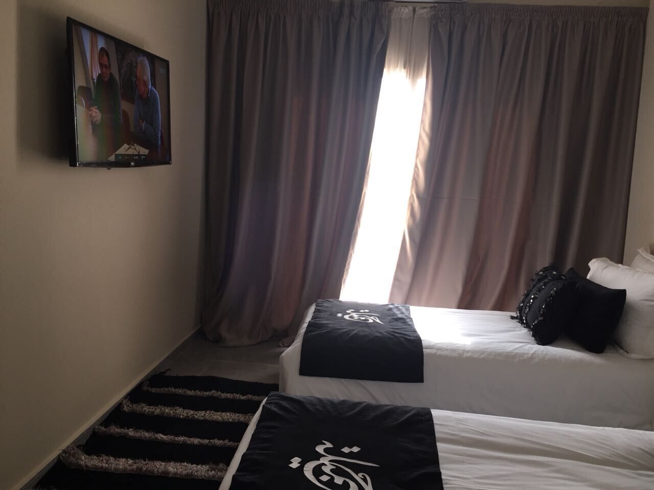 A hotel room with two beds, a TV on the wall, and a window with curtains.