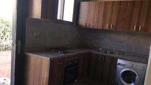Une cuisine compacte avec des meubles en bois, un four encastré, une cuisinière à gaz et un lave-linge à chargement frontal.