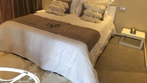Un lit bien fait, recouvert d’une couverture blanche et marron, avec deux oreillers moelleux et une petite table de chevet sur laquelle se trouvent un livre et une lampe.