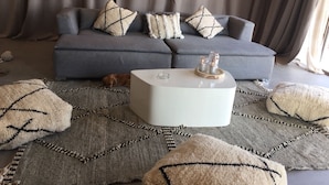 Un salon avec un canapé gris, des coussins décoratifs à motifs, une table basse blanche et un grand tapis tissé.