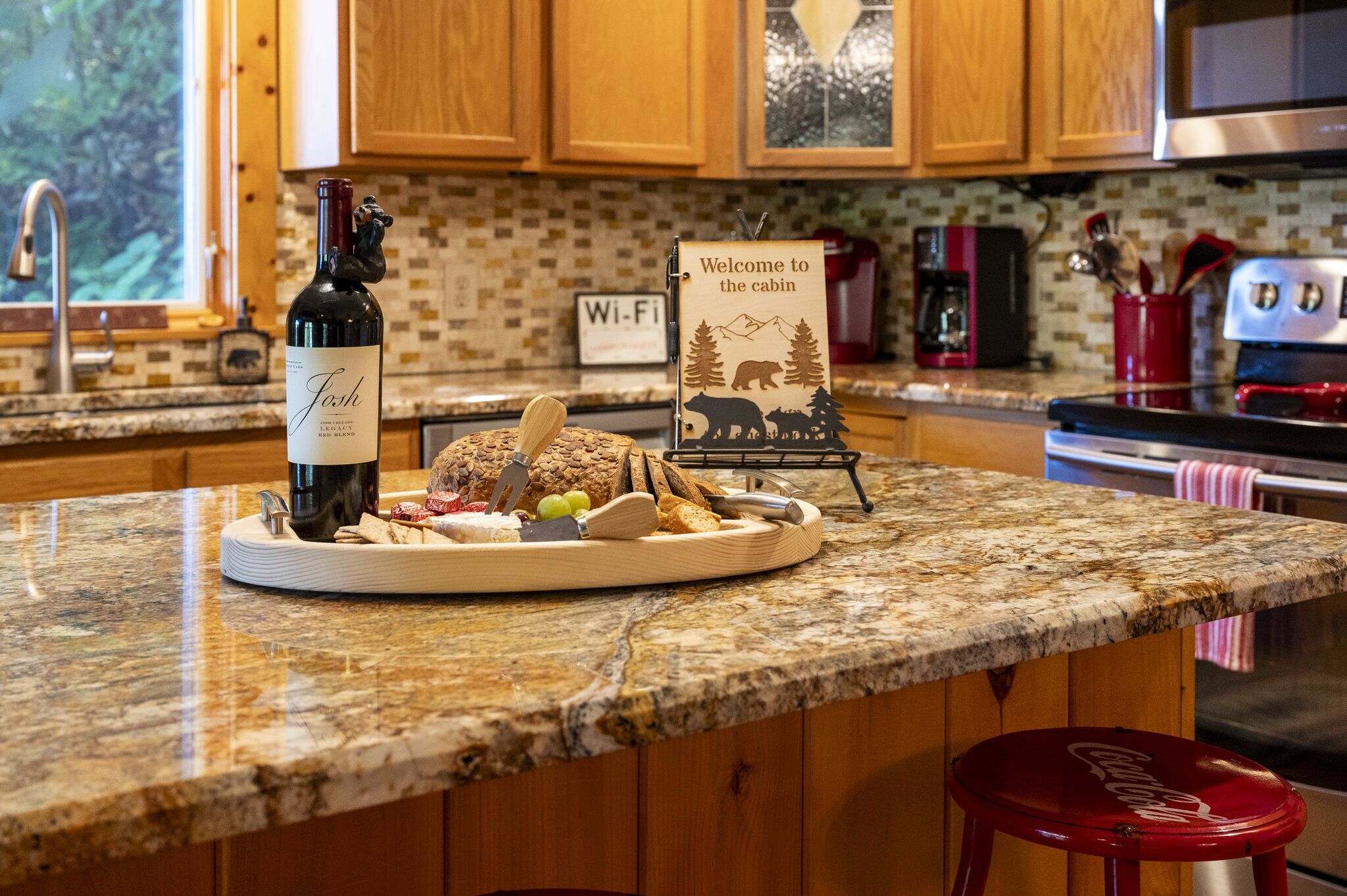 A kitchen counter with a wine bottle, a welcome sign, and a plate of food.