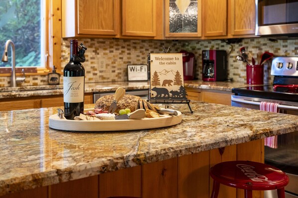 A kitchen counter with a wine bottle, a welcome sign, and a plate of food.