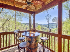 Une terrasse en bois avec une table ronde, un tabouret de bar et une bouteille de vin.