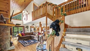 A spacious living area with a stone fireplace, a wooden staircase, and a cozy seating area with a large couch and a coffee table. - Long- & Short-Range Views/King Beds/Fireplace/Fire Table/Game Room (Maggie Valley)