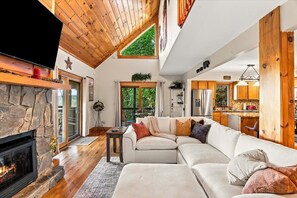 A spacious living room with a stone fireplace, a large sectional sofa, and a wooden ceiling.