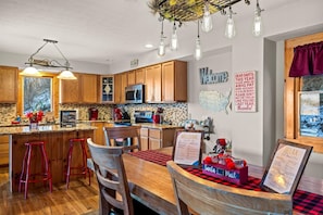 A modern kitchen with wooden cabinets, a central island with stools, a 'Welcome' sign, and a 'Relax' sign.