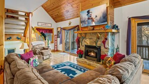 A cozy living room with a fireplace, wooden beams, a sofa, and a television. - Long- & Short-Range Views/King Beds/Fireplace/Fire Table/Game Room (Maggie Valley)