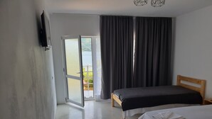 Et soveværelse med seng, TV ophængt på væggen, en skydedør til en balkon og et vindue med gardiner.