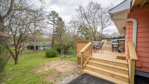 A wooden deck with steps leading to a covered patio area, surrounded by trees and a grassy yard. - NEW! Completely renovated 2bed/1bath UPTOWN home! (Hot Springs National Park)