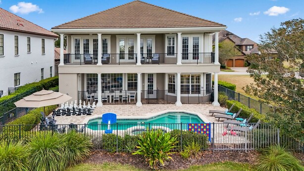 Une maison à deux étages avec une grande véranda à l’avant, une piscine et un jardin clôturé à l’arrière.