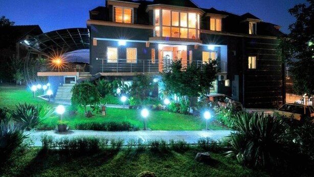 Una casa moderna de dos pisos con un patio delantero bien iluminado, un espacio exterior cubierto y un coche estacionado en la entrada.