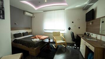 A modern hotel room with a bed, a desk, a chair, and a TV.