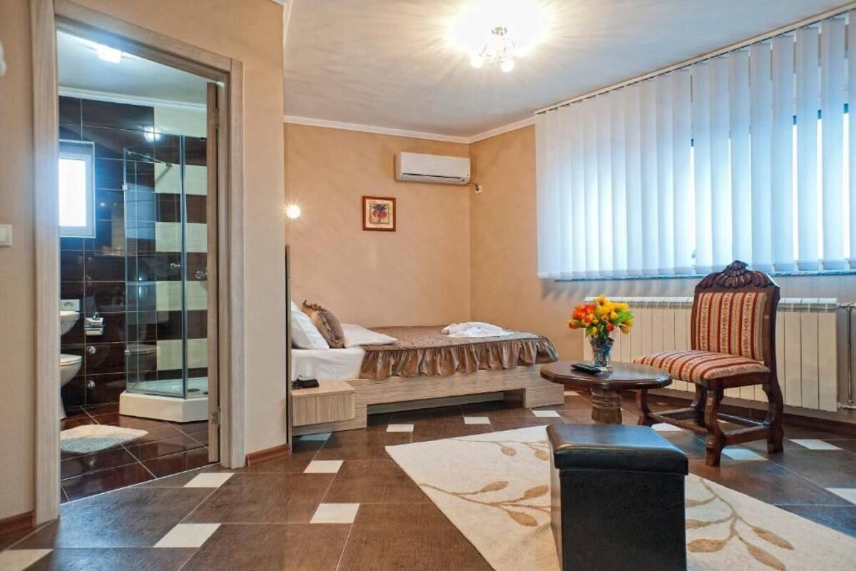 A modern bedroom with a bed, a chair, a small table with flowers, and a window with blinds.