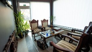 Una habitación con dos sillas de madera y una mesa, una planta en maceta y una puerta con un cartel.